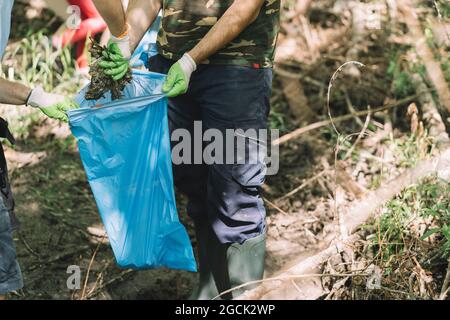 Gruppo di bambini attivi sociali con l'uomo volontario raccogliere i rifiuti in sacchetto di rifiuti durante la campagna ambientale in natura estiva Foto Stock