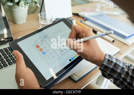 Le mani del progettista dell'interfaccia utente disegnano lo schizzo dell'applicazione mobile sul computer tablet e scelgono la tavolozza dei colori Foto Stock