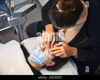 Donna allegra in attesa in abito ornamentale seduta su palla yoga con vestiti per bambini contro la commode in camera Foto Stock