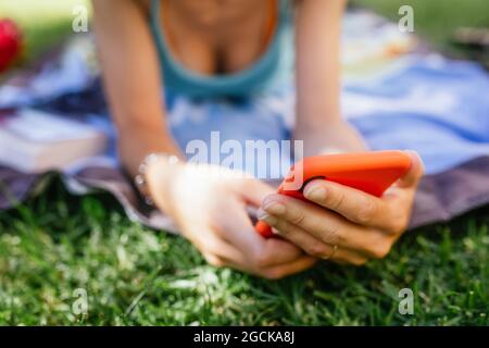 Vista ravvicinata di una persona anonima che usa il telefono mentre si sdraierà sull'erba in una giornata estiva Foto Stock