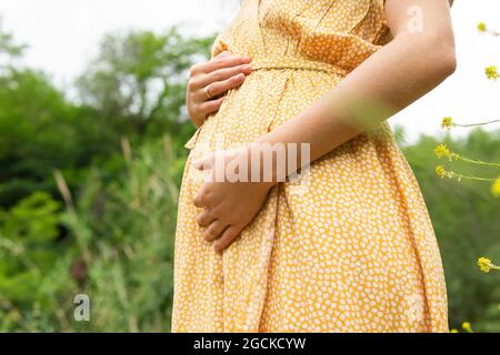 Vista laterale del raccolto anonimo donna incinta in estate vestito che tocca la pancia mentre si trova in campo in campagna Foto Stock