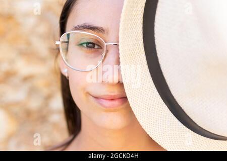 Primo piano ritratto di giovane donna in occhiali che coprono metà faccia con un cappello mentre si guarda la macchina fotografica Foto Stock