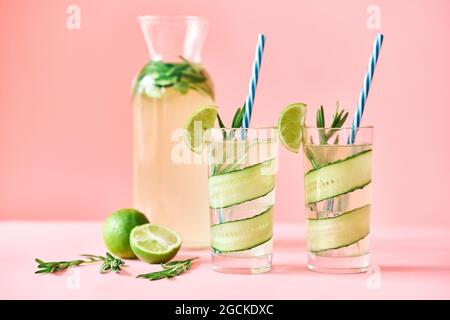Cocktail rinfrescanti freddi con lime, cetrioli, rosmarino e ghiaccio in vetro su sfondo rosa. Festa, concetto estivo Foto Stock