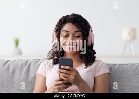 Guarda video divertenti e naviga in Internet, impara l'inglese a casa, studia, impara e rilassati a casa. Felice giovane afroamericana femmina in hea wireless Foto Stock