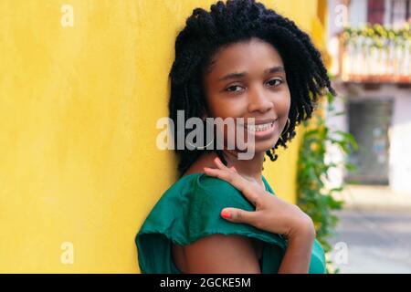 Chiudi ritratto a testa in alto di una bella giovane donna nera sorridente appoggiata al muro esterno Foto Stock