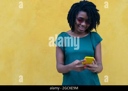Felice giovane donna che controlla il suo cellulare per strada Foto Stock