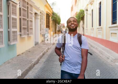 Uomo africano sorridente con zaino che guarda in alto mentre si alza in piedi all'aperto Foto Stock