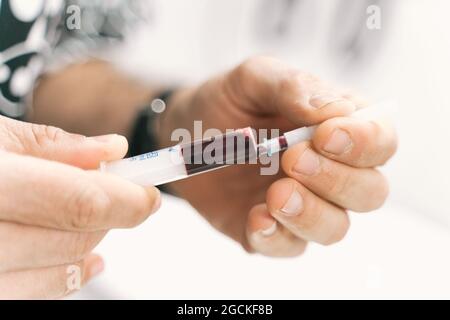 Closeup medico anonimo con siringa e provetta con campione di sangue del paziente per la ricerca diagnostica in laboratorio di clinica veterinaria Foto Stock