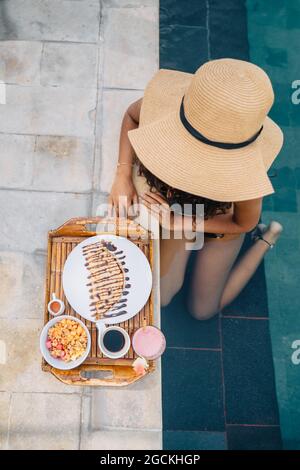 Vista laterale della giovane donna domenicana alla moda millennial con lunghe trecce afro seduti sul pavimento e guardando lontano mentre si ascolta la musica in headpho Foto Stock