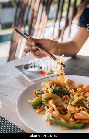 Anonimo turista femminile con deliziosa pasta tra bastoncini di cibo sopra la tavola con salsa di soia e fette di zenzero sottaceto all'aperto Foto Stock