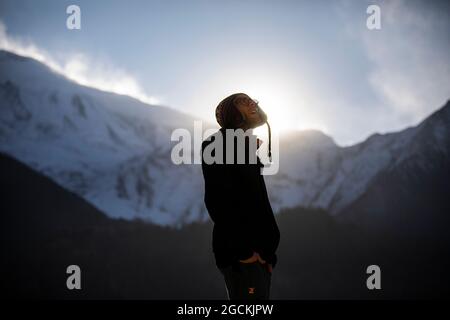 Vista laterale del sorridente viaggiatore maschile in abiti caldi in piedi sullo sfondo della catena montuosa dell'Himalaya nella giornata di sole in Nepal Foto Stock