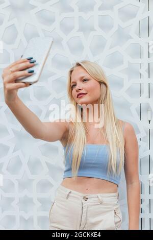 Donna bionda con capelli biondi che si autogirano sul telefono cellulare in città strada Foto Stock