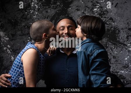 Multietnico amante Donna e figlio adolescente baciare l'uomo sulla guancia su sfondo scuro in studio Foto Stock