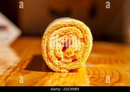 Tovagliolo giallo in microfibra a tre strati arrotolato su una superficie di legno Foto Stock