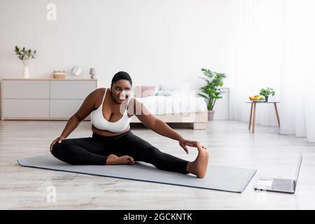 Pump nero signora allungare gambe, praticare yoga sul tappetino, seguendo tutorial sul computer portatile, facendo esercizi online a casa Foto Stock