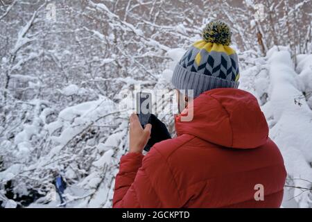 Da dietro un uomo che scatta foto con il suo cellulare del compagno in un paesaggio innevato Foto Stock