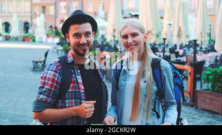 Zoom di turisti che tengono la mappa e sorridono alla fotocamera. Si trova su una grande piazza del mercato della vecchia città europea. Foto Stock