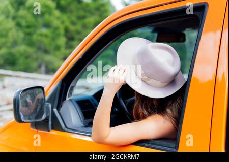 Vista laterale del viaggiatore femminile seduto sul sedile del conducente in pulmino e godendo di un viaggio su strada in estate Foto Stock