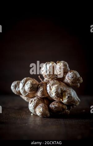 Composizione di vita still con tuberi di carciofo di Gerusalemme chiamato anche radice solare o topinambur olaced su tavola di legno contro sfondo nero Foto Stock