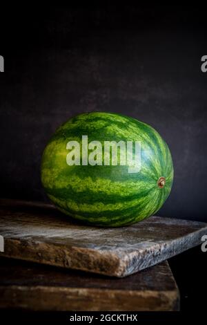 Ancora vita composizione di tutto filodiffusione verde a righe mature posto su tavola rustica di legno contro sfondo nero Foto Stock