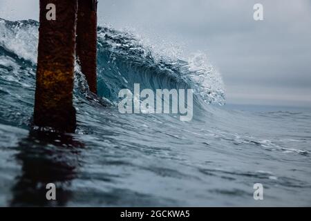 Un'onda vetrosa che si schiantano sulla spiaggia. Infrangendo l'onda dell'oceano e il vecchio molo Foto Stock