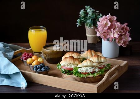Deliziosi panini con croissant e verdure serviti su vassoio con cappuccino e succo d'arancia preparati per la colazione francese e messi su un tavolo di legno Foto Stock