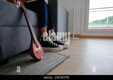 Crop Unriconoscable African American femmina musicista seduto sul divano vicino mandolino Foto Stock