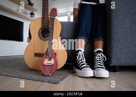 Crop Unriconoscable African American femmina musicista seduto sul divano vicino chitarra acustica e mandolino Foto Stock