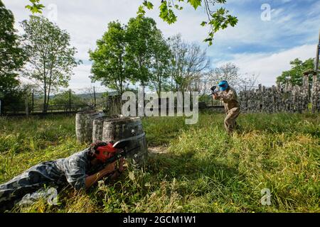 Giocatori di squadra irriconoscibili in camouflage indossare e con le pistole che si puntano l'un l'altro mentre si gioca paintball Foto Stock