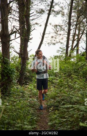 Raccolto senza volto viaggiatore maschile in abiti casual toccando tronco di albero durante il viaggio escursionistico nella foresta in giorno di sole Foto Stock