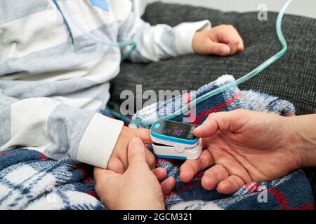 Crop Unrecognized Woman usando il pulsossimetro moderno sul dito del bambino per misurare il livello di ossigeno nel sangue Foto Stock