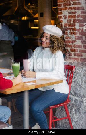 Ritratto di una donna afro con un cappello bere un frullato all'interno di un bar Foto Stock