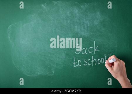 Le insegnanti donne scrivono a mano sul bordo della scuola di ritorno al gesso bianco della scuola. Concetto di ritorno a scuola. Fatevi beffare per il design. Spazio di copia. Concetto di istruzione. Foto Stock