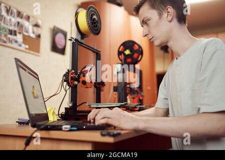 Basso angolo di concentrato giovane maschio browser modello 3D su computer portatile prima di stampare mentre si siede a tavola e lavora in studio Foto Stock