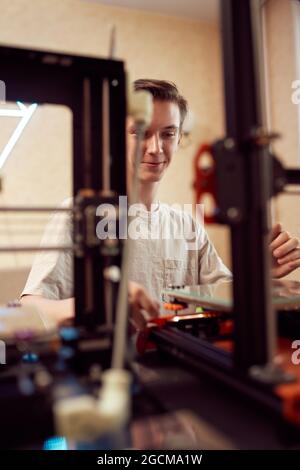 Angolo elevato di controlli di regolazione maschili anonimi sulla stampante 3D durante la creazione di un modello in plastica in officina Foto Stock