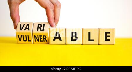 Simbolo vulnerabile o variabile. L'uomo d'affari gira i cubi di legno e cambia la parola vulnerabile a variabile. Splendido sfondo bianco, spazio per la copia. Autobus Foto Stock