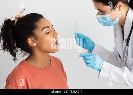 Infermiere che prende tampone orale per il campione di coronavirus da donna nera Foto Stock