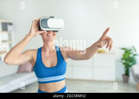 Donna sorridente con visore VR che si allena a casa Foto Stock