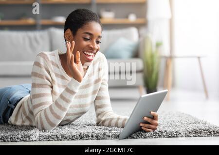 Black Lady positivo con il tablet digitale che effettua la videochiamata a casa Foto Stock