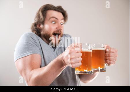 Ritratto di un felice giovane uomo bearded che tiene due tazze di birra isolate su sfondo grigio chiaro Foto Stock