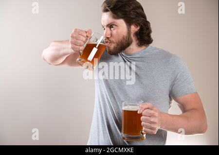 Uomo bere birra isolato su sfondo grigio chiaro Foto Stock