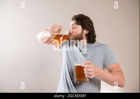 Uomo bere birra isolato su sfondo grigio chiaro Foto Stock