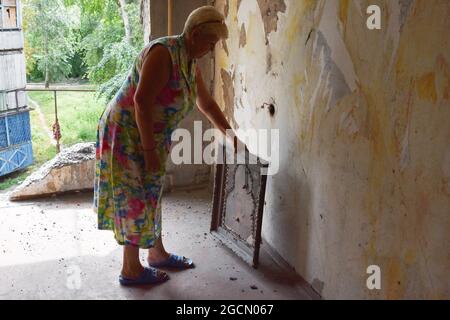 Krasnogorivka, Ucraina. 8 agosto 2021. Una donna si trova nella sua stanza distrutta con l'icona ortodossa che è stata fatta a mano dal suo marito gravemente ferito. Un condominio residenziale a Krasnogorivka, è stato abbattuto la mattina del 5 agosto. Un civile è stato gravemente ferito nel suo appartamento. Il conflitto armato nell'Ucraina orientale continua a pagare un tributo elevato ai civili, dalla minaccia alla loro sicurezza fisica alla limitazione dell'accesso a cibo, medicinali, alloggi adeguati e scuole. Credit: SOPA Images Limited/Alamy Live News Foto Stock