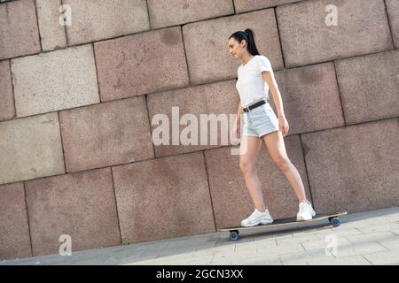 Bella giovane skater donna a cavallo sulla sua longboard in città. Foto Stock