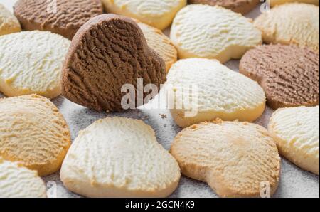 Un sacco di biscotti colorati a forma di cuore su una teglia da forno, il cioccolato è sul bordo. Foto Stock