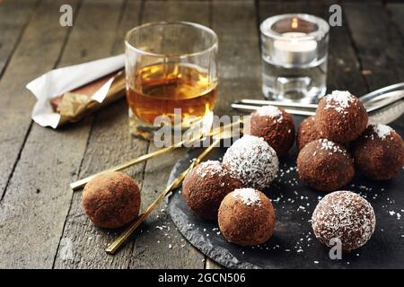 Palle di rum al cioccolato con fiocchi di cocco, dolci caramelle su sfondo scuro. Foto Stock