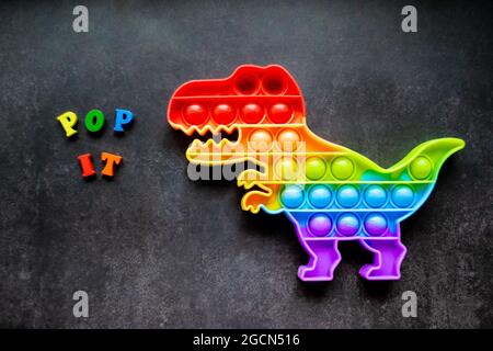 Giocattolo pop esso dinosauro arcobaleno colori su uno sfondo nero con lettere multicolore e lettere - Pop it. Foto Stock