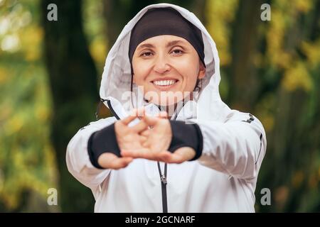 Una donna atletica sorridente che indossa una moderna giacca impermeabile che strizza polsi e dita nel colorato verde giallo parco autunnale. spo attiva Foto Stock