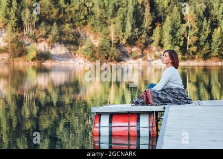 Donna di mezza età sul molo di legno sulla montagna godendo di acque tranquille del lago durante la sua passeggiata nel periodo di stagione autunnale. Tempo libero all'aperto in n Foto Stock