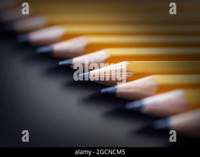 Una fila di matite gialle disposte in diagonale su uno sfondo nero. Messa a fuoco selettiva. Foto Stock